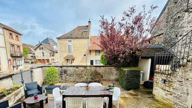 A courtyard with a wooden table and white chairs, surrounded by stone walls and a stone building.