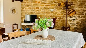 A rustic room with a stone wall, a television, a dining table with a white tablecloth, and a vase with flowers.