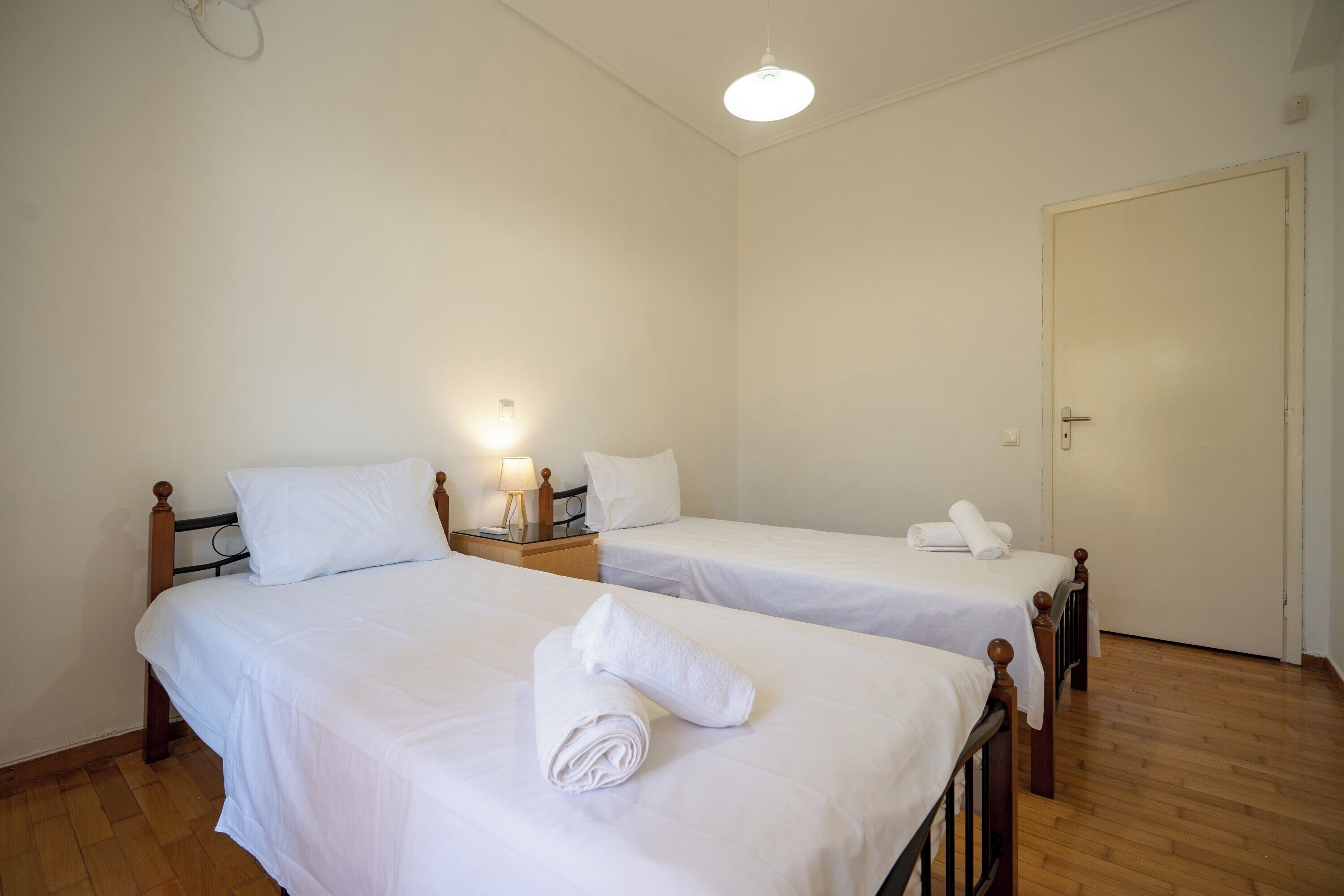 Une chambre d’hôtel avec deux lits simples, des têtes de lit en bois, du linge de lit blanc, une lampe de chevet et un plancher en bois.