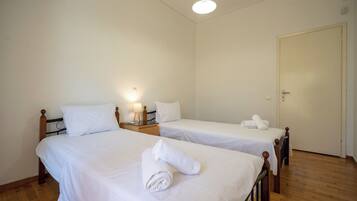 Une chambre d’hôtel avec deux lits simples, des têtes de lit en bois, du linge de lit blanc, une lampe de chevet et un plancher en bois.