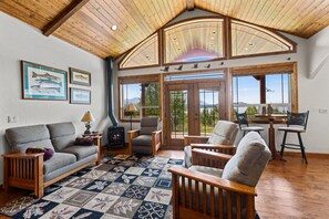 A cozy living room with a fireplace, comfortable seating, large windows, and a view of the outdoors.