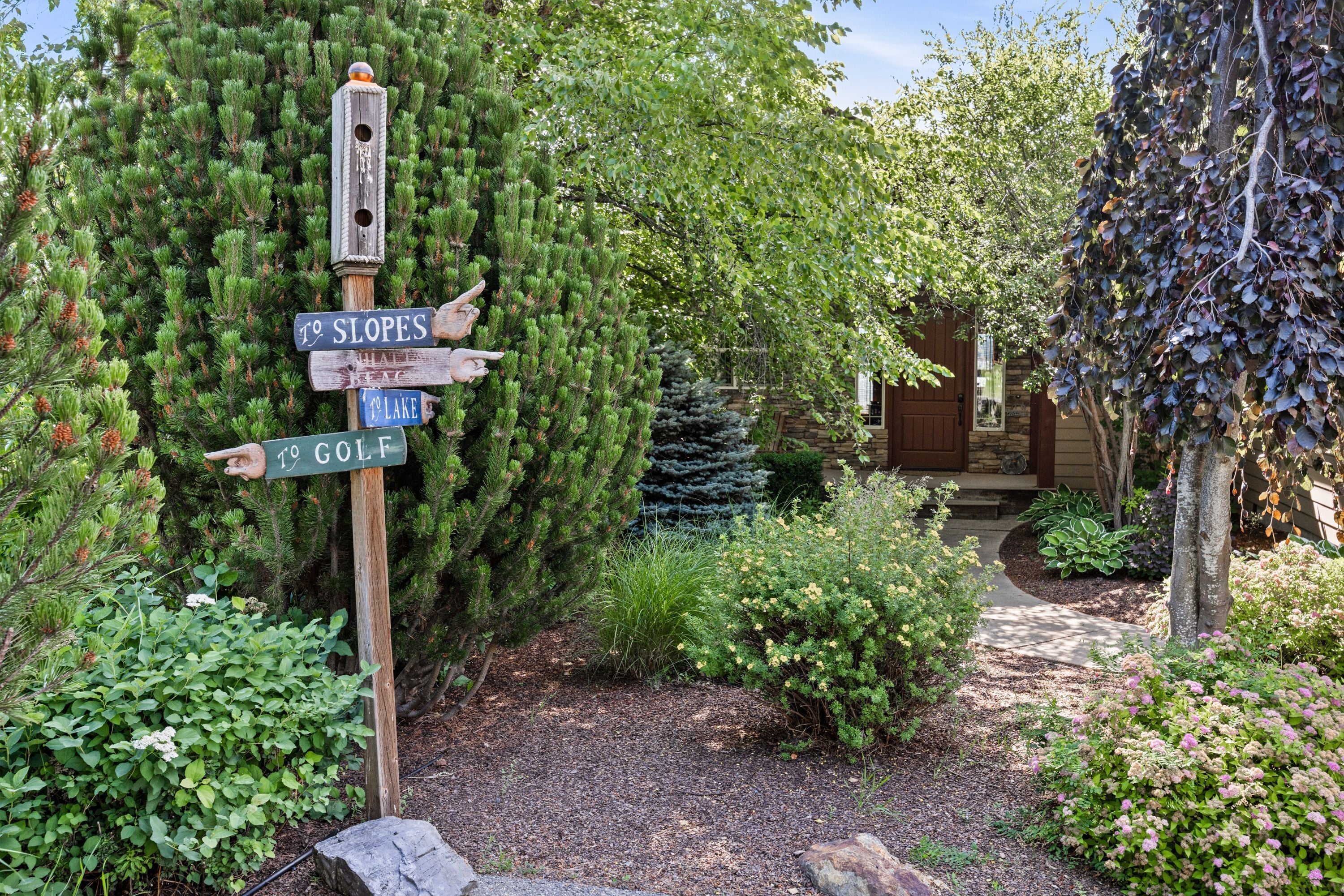 A wooden signpost with directional arrows, surrounded by lush greenery and a garden path.