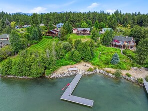 A lakeside property with a dock, multiple houses, and a forested hillside.
