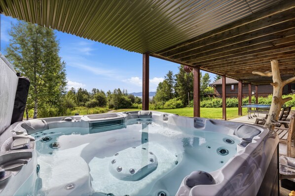 A hot tub with a wooden deck and a view of a house in the background.