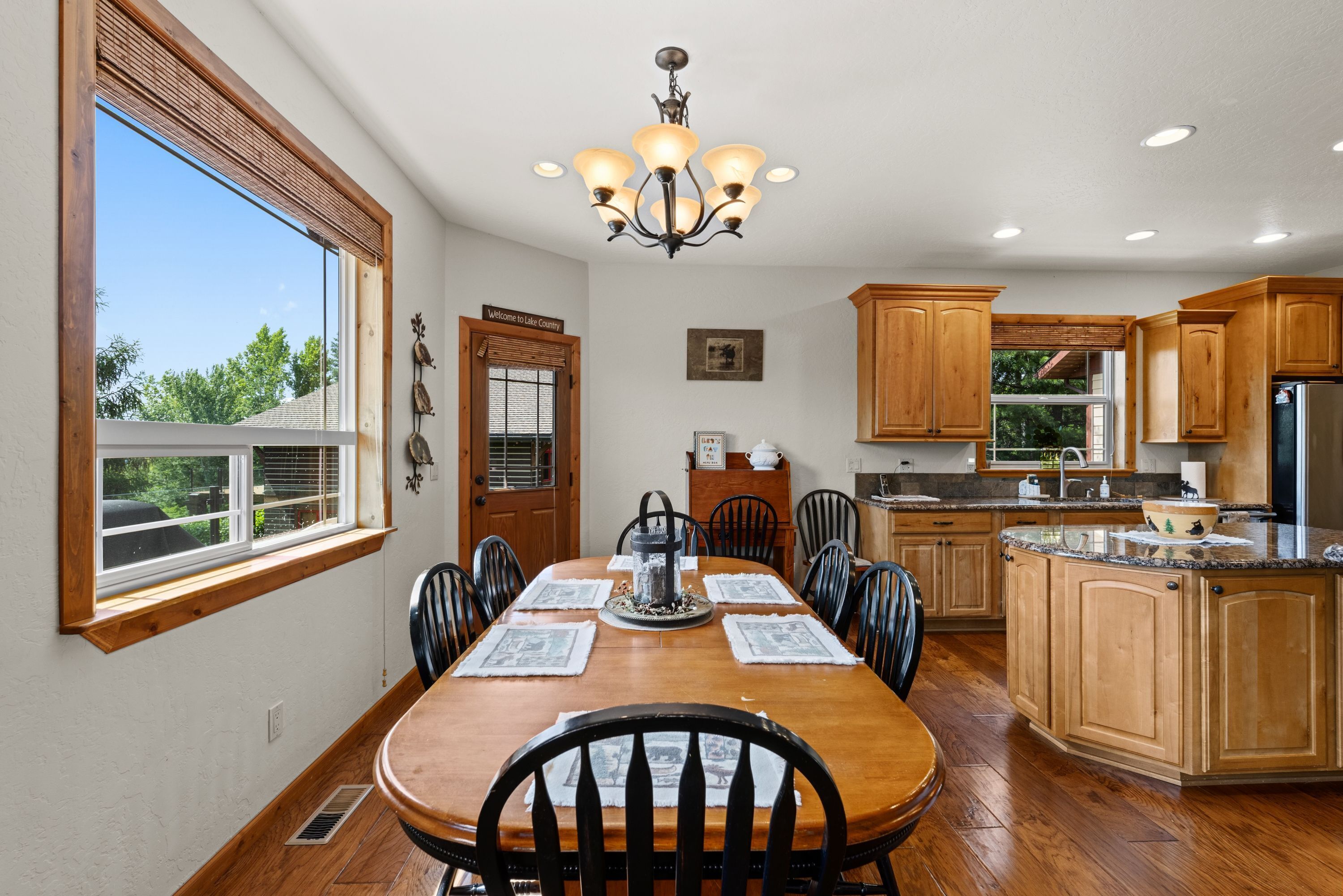 A spacious kitchen with wooden cabinets, a dining table with chairs, and a large window.