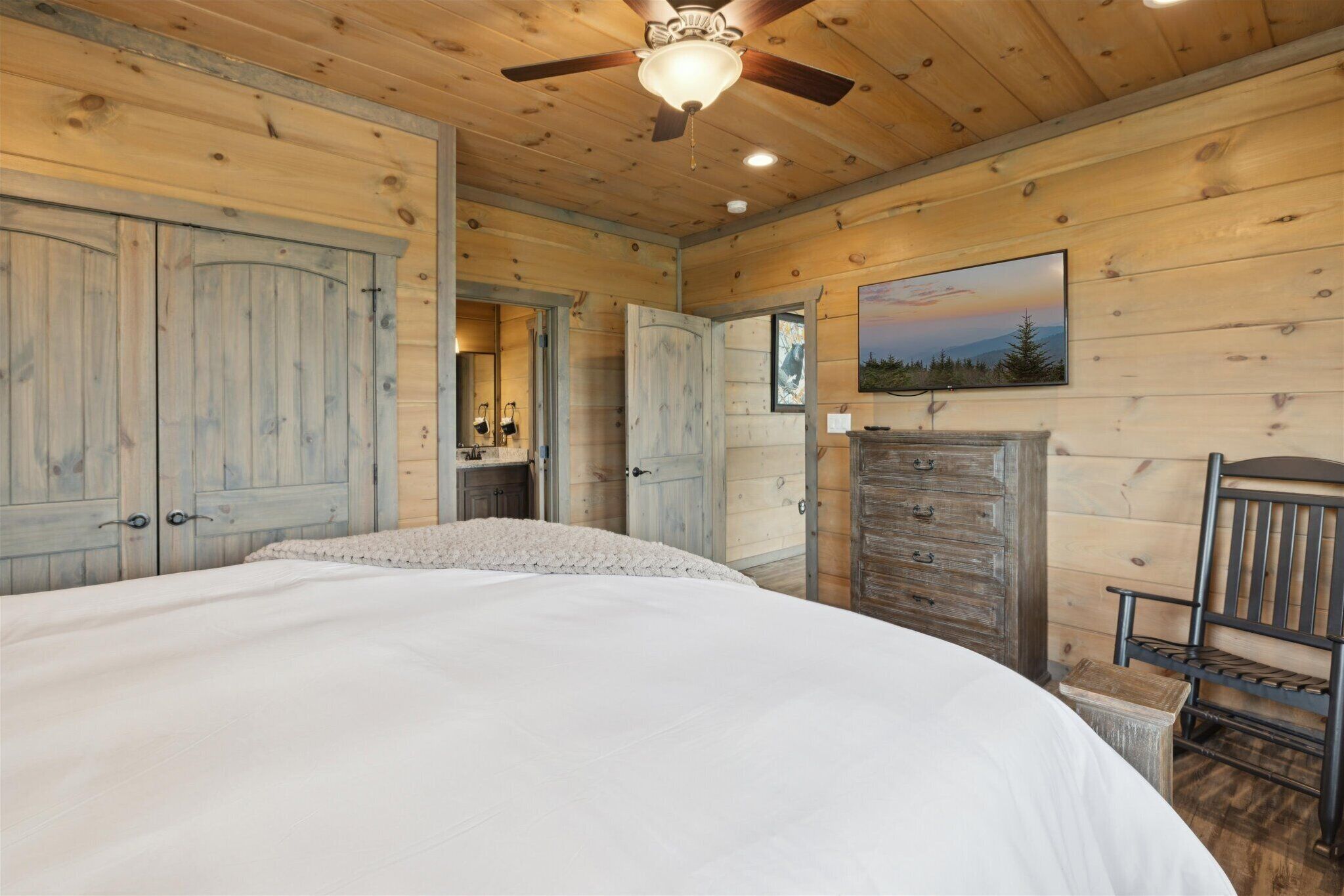 Quarto de cabana de madeira com cama, penteadeira e ventilador de teto.