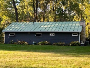 A single-story building with a green metal roof, a small window, and a brick chimney.