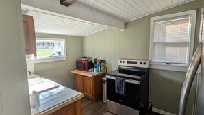 A compact kitchen with a wooden countertop, a built-in microwave, a stove, and a window with blinds. - The Cottage at River's Bend (Howard)
