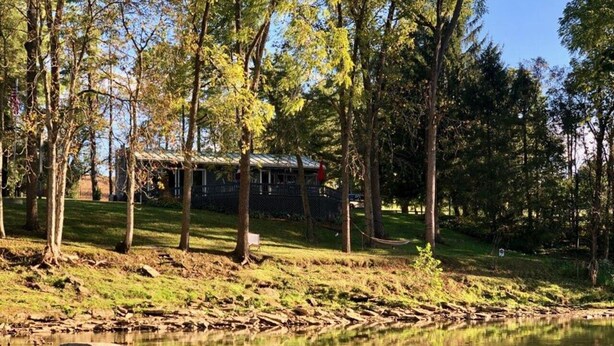 A lakeside cabin with a deck overlooking the water, surrounded by trees. - The Cottage at River's Bend (Howard)