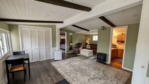 A spacious living area with a dining table, a patterned rug, and a kitchen visible through an open doorway. - The Cottage at River's Bend (Howard)