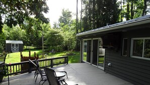 A deck with outdoor furniture and a building with large windows. - The Cottage at River's Bend (Howard)