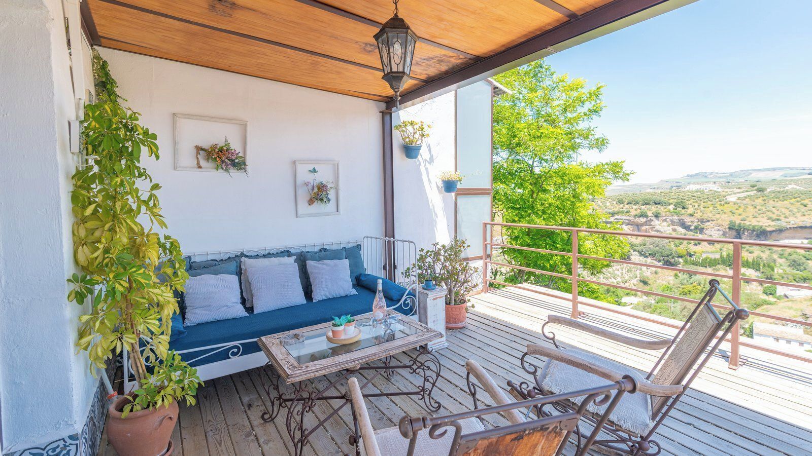 A balcony with a wooden ceiling, a blue sofa, a glass coffee table, and metal chairs.