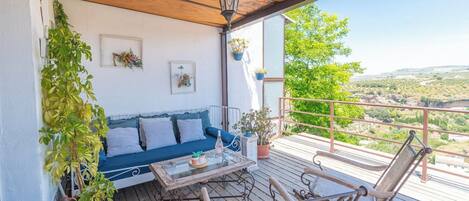 A balcony with a wooden ceiling, a blue sofa, a glass coffee table, and metal chairs.