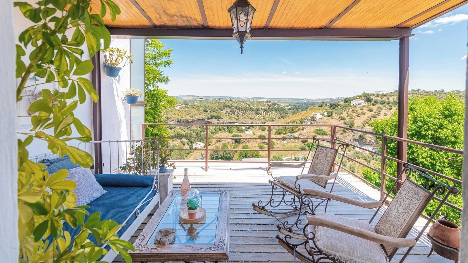 Ein Balkon mit einem Bett, zwei Stühlen, einem Tisch und Blick auf eine hügelige Landschaft.
