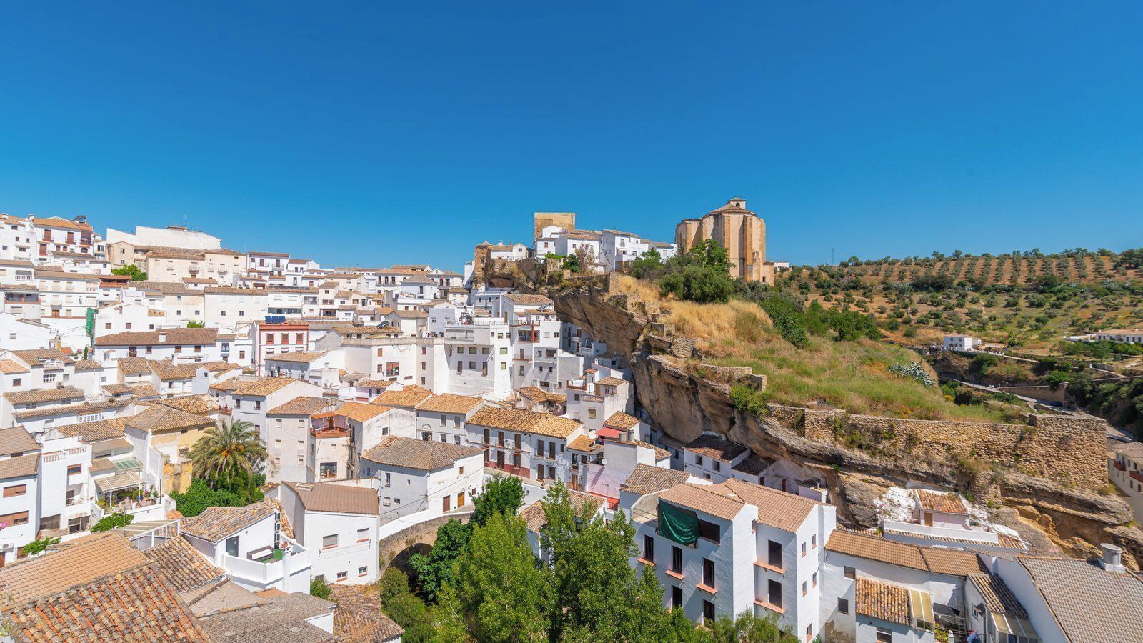 A coastal town with white buildings, a prominent rock formation, and a church.