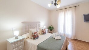 Un dormitorio con cama, mesitas de noche, lámpara, planta en maceta y televisor.
