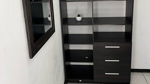 Un armario de madera oscura con varios estantes y cajones, ubicado frente a una pared blanca con un espejo encima.