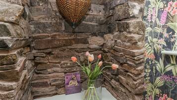 Esquina de pared de piedra con una cesta tejida, un jarrón de cristal con tulipanes, un cartel enmarcado y una toalla rosa.