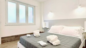 Een moderne hotelkamer met een groot bed, een houten vloer, een raam met zonwering en een tv aan de muur.