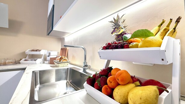 Een keuken met een roestvrijstalen spoelbak, een wit aanrecht en een mand met fruit.