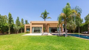 Une maison moderne dotée d’une piscine, entourée d’une pelouse bien entretenue et de palmiers.