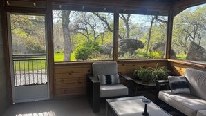 Een overdekt terras met uitzicht op een bebost landschap, een bank, een loungebank en een bijzettafeltje.