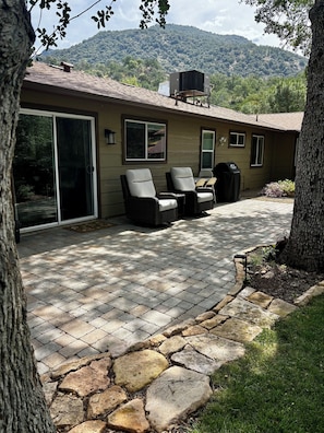 Una casa con patio, due sedie, un barbecue e vista su una collina boscosa.