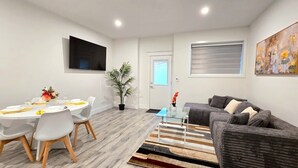 Una sala de estar moderna con un sofá gris, una mesa de centro de cristal y un comedor con una mesa redonda y sillas.