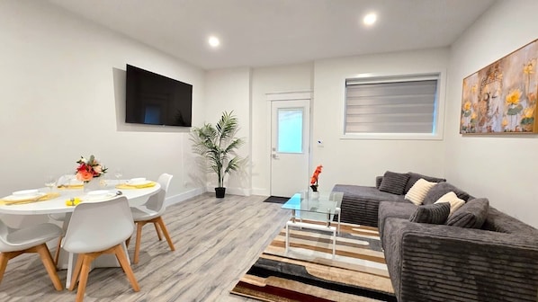 A modern living room with a grey sofa, a glass coffee table, and a dining area with a round table and chairs.