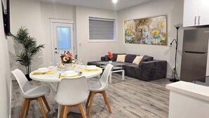Una cocina moderna con horno empotrado, un comedor con mesa redonda y sillas, y un sofá gris.