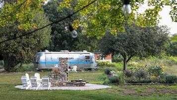A stationary RV with a stone fireplace and outdoor seating in a garden setting.