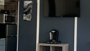 A modern living room with a flat-screen TV mounted on the wall, a ceiling fan, and a wooden coffee table. - Argyles Too! A brand new Loft Efficiency (Kitty Hawk)