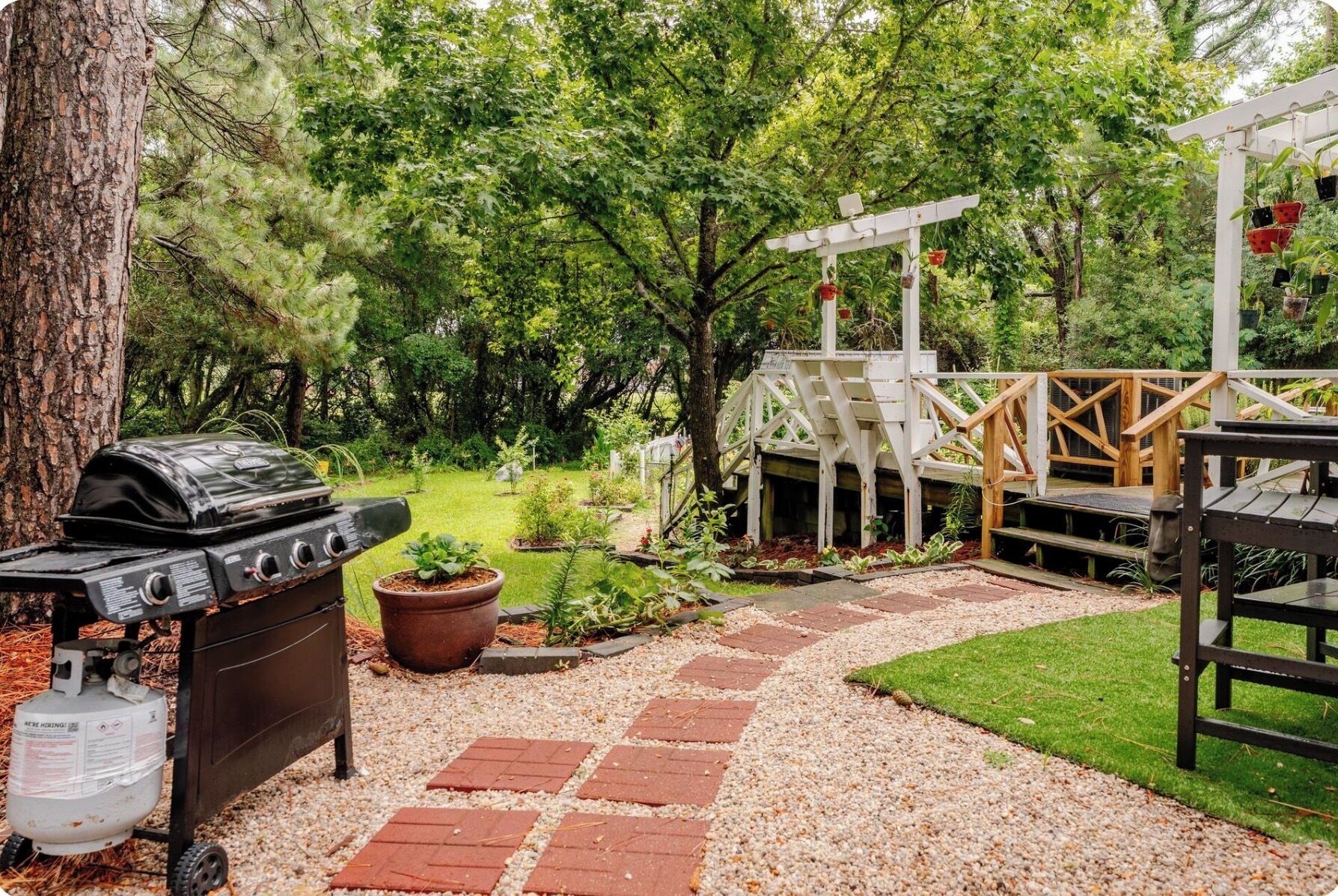 A backyard with a barbecue grill, a wooden pergola, and a gravel pathway.