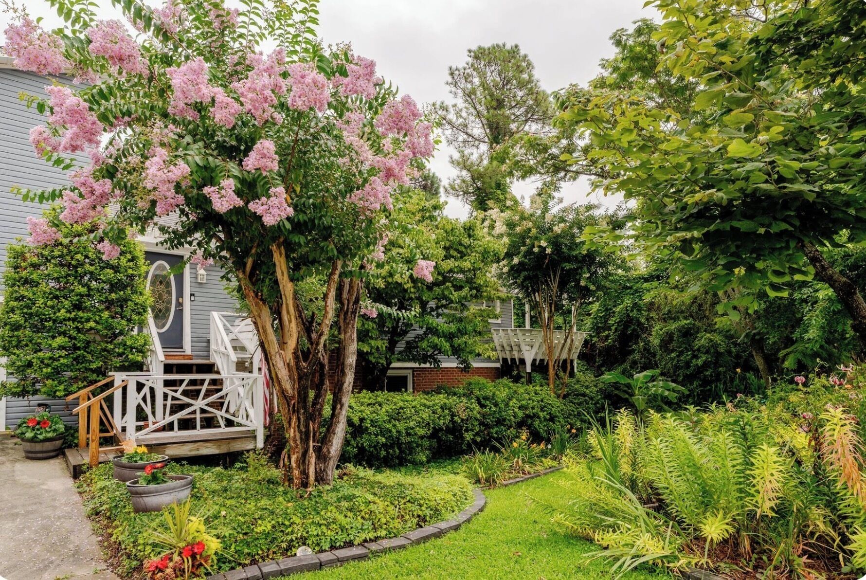 A garden with a white gazebo, a tree with pink flowers, and various plants.