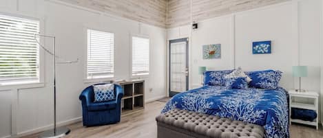 Un dormitorio con cama, una silla, un banco, un ventilador de techo y una puerta.