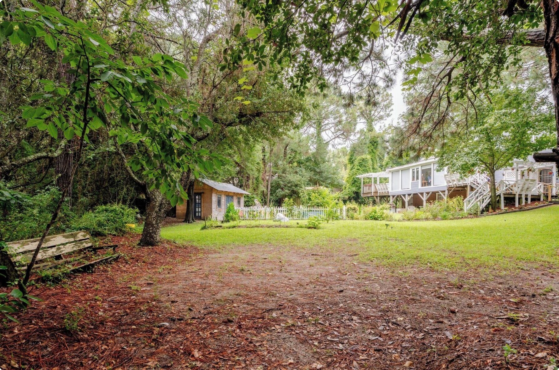 A wooded area with a small cabin and a larger house with a porch.