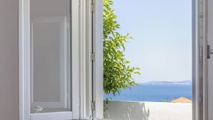 Quarto com vista para o mar, porta branca, mesa preta com um vaso branco e cadeiras de vime.