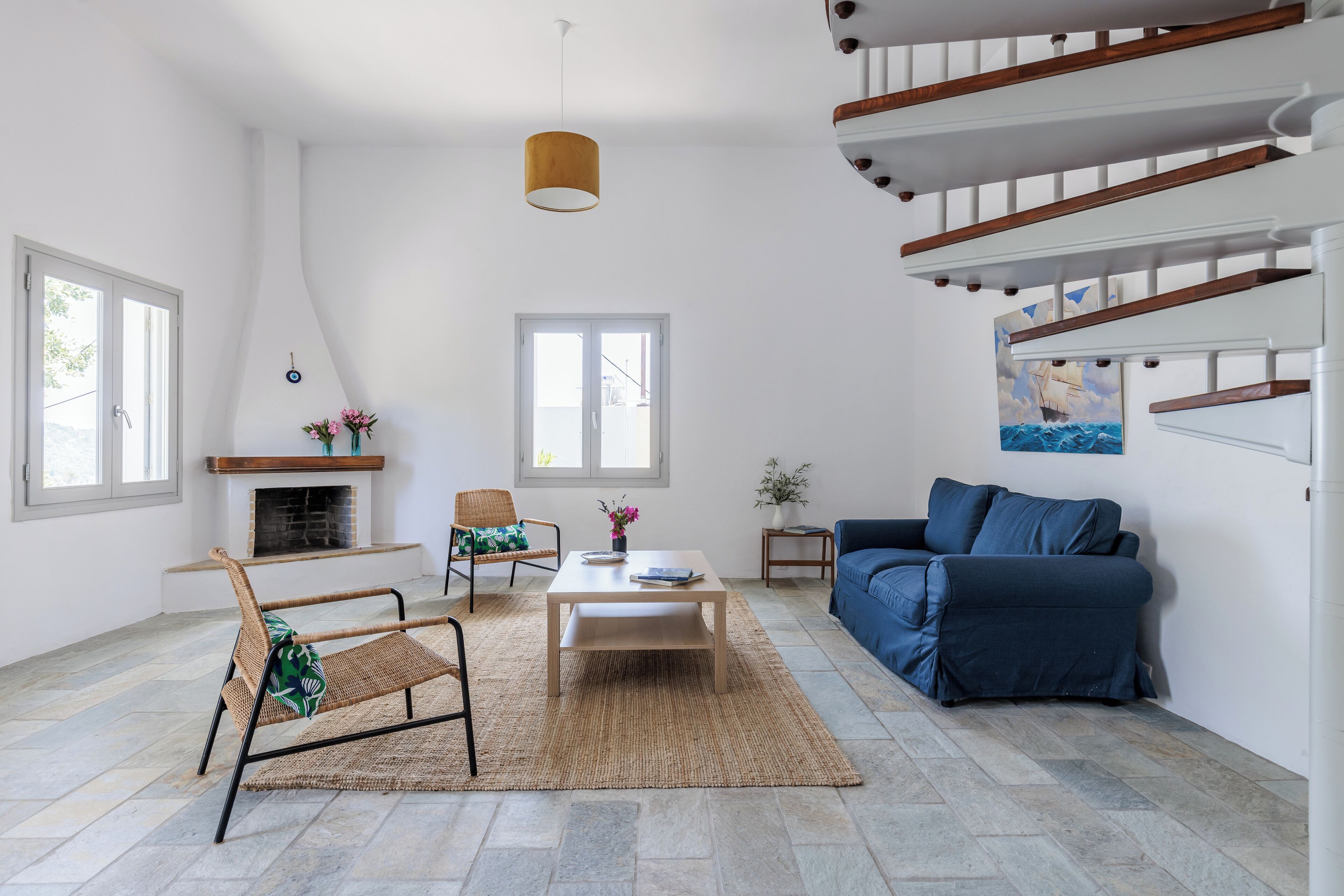 Un salon spacieux avec une cheminée, un canapé bleu, une table basse en bois et un fauteuil en osier.