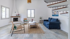 Uma sala de estar ampla com lareira, um sofá azul, uma mesa de centro de madeira e uma poltrona de vime.