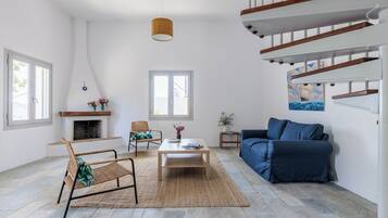 Un salon spacieux avec une cheminée, un canapé bleu, une table basse en bois et un fauteuil en osier.