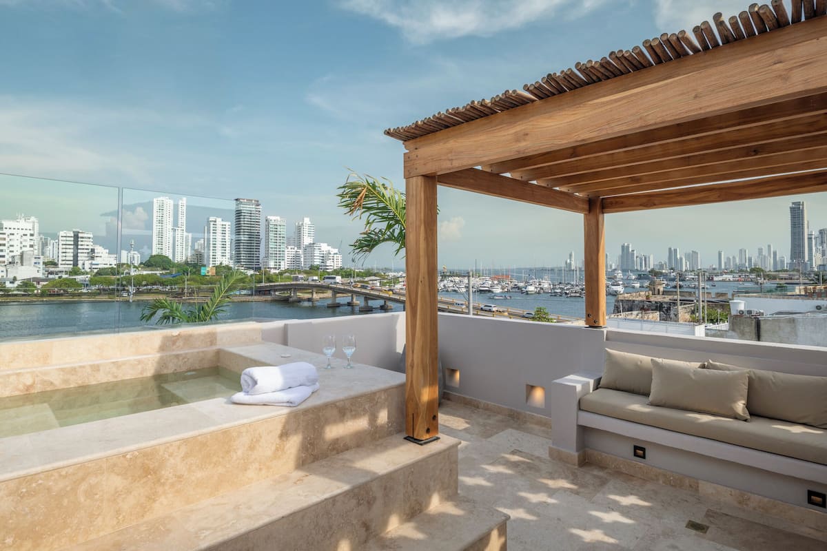 A rooftop terrace with a wooden pergola, a hot tub, and a seating area with cushions.