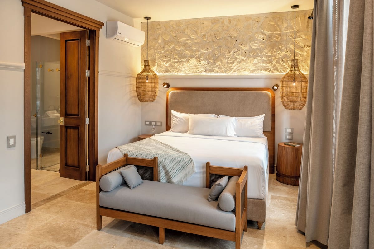 A modern bedroom with a large bed, a wooden bench, and two wall-mounted lamps.