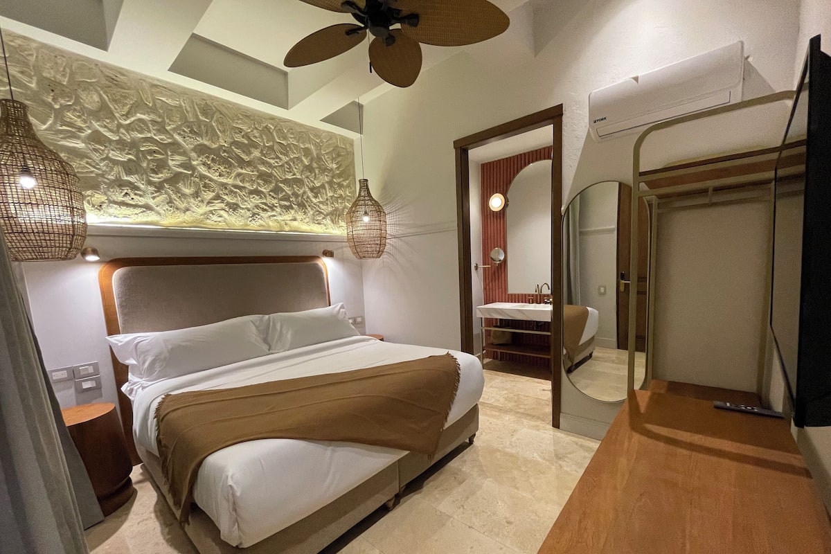 A modern bedroom with a bed, bedside tables, a ceiling fan, and a bathroom with a mirror and sink.