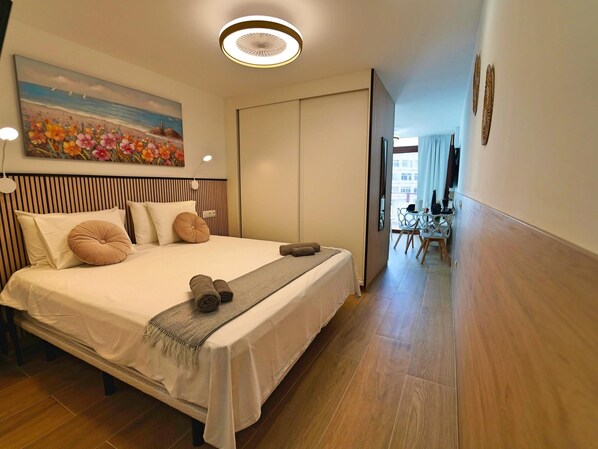 A hotel room with a bed, a painting, a desk, and a chair.