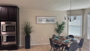 Un coin repas avec une table dressée pour quatre personnes, entourée de chaises, d’une plante en pot et d’un tableau accroché au mur.