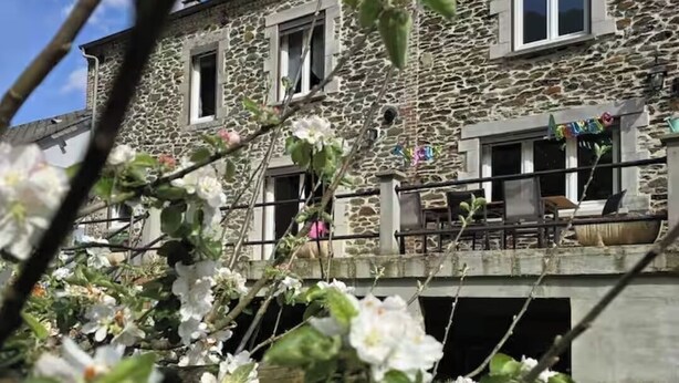 Un bâtiment en pierre doté de nombreuses fenêtres et de balcons, entouré de verdure et de plantes en fleurs.