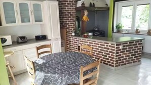 Une cuisine avec un mur d’accent en briques, un coin repas avec une table et des chaises, et une fenêtre donnant sur un paysage verdoyant.