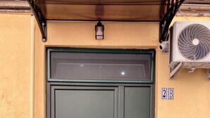 Une porte verte avec une petite fenêtre au-dessus, une boîte aux lettres et un climatiseur fixé au mur.