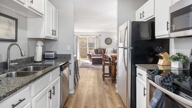 A modern kitchen with white cabinets, granite countertops, and stainless steel appliances. There is a dining area with a wooden table and chairs. - Tranquil Getaway For 8 (Branson)