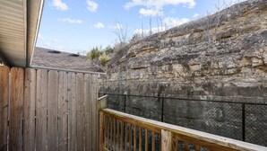 A wooden deck with a stone wall backdrop and a metal fence. - Tranquil Getaway For 8 (Branson)